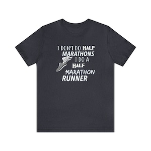 May include: Dark gray t-shirt with white text that reads "I DON'T DO HALF MARATHONS I DO A HALF MARATHON RUNNER." A graphic of a running shoe with wings is above the text. The shirt is a crew neck.