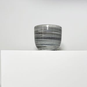 May include: A small, rounded ceramic planter or bowl featuring a swirling, marbled pattern of black, gray, and white horizontal lines. The vessel has a smooth, glossy finish and a simple, cylindrical shape with a slightly tapered base.