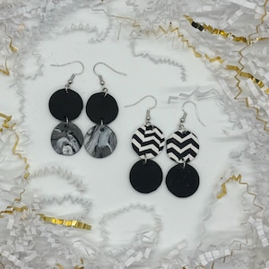 May include: Two pairs of black and white dangle earrings. One pair features black and white marbled circles and the other pair features black and white chevron circles.