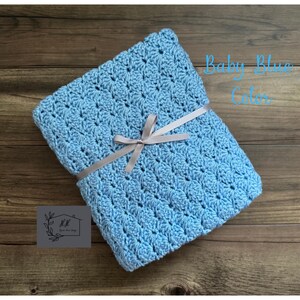 Puede incluir: Una manta de ganchillo azul beb&eacute; atada con una cinta gris. La manta est&aacute; doblada y tiene un patr&oacute;n texturizado. El texto en la imagen dice "Baby Blue Color".