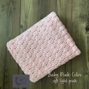 Puede incluir: Una manta de ganchillo rosa beb&eacute; con un patr&oacute;n texturizado. La manta est&aacute; doblada y descansa sobre una superficie de madera. El texto en la imagen dice "Baby Pink Color soft light pink".
