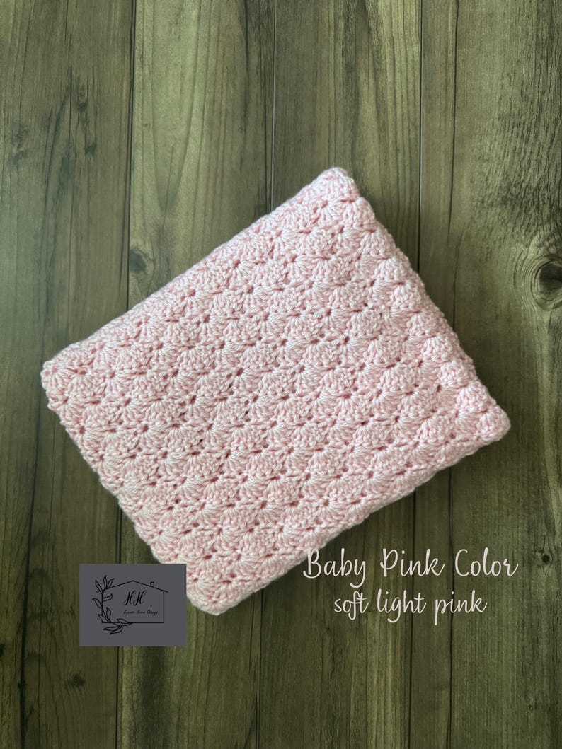 Puede incluir: Una manta de ganchillo rosa beb&eacute; con un patr&oacute;n texturizado. La manta est&aacute; doblada y descansa sobre una superficie de madera. El texto en la imagen dice "Baby Pink Color soft light pink".