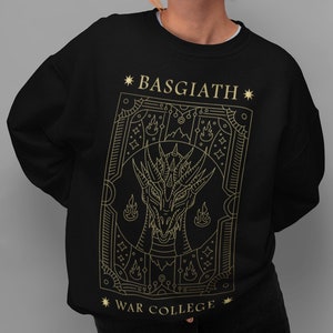 Peut inclure: Sweat-shirt noir avec un contour doré d'un dragon et le texte "*BASGIATH*" et "*WAR COLLEGE*"