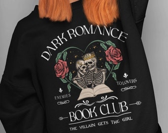 May include: Black sweatshirt with the text "DARK ROMANCE BOOK CLUB" and a graphic of two skeletons embracing, wearing crowns, and surrounded by roses. The text "ENEMIES TO LOVERS" and "THE VILLAIN GETS THE GIRL" are also included.