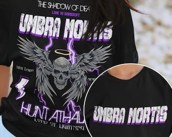 May include: Black t-shirt with a purple and white graphic print of a skull with wings and the text "UMBRA MORTIS" on the back. The front of the shirt has the text "UMBRA MORTIS" in purple.