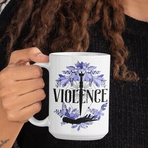 以下が含まれることがあります： 白いセラミック製のマグカップで、紫色の花柄と黒い「VIOLENCE」の文字が書かれています。デザインの中央には、ナイフを持った手の黒いシルエットがあります。