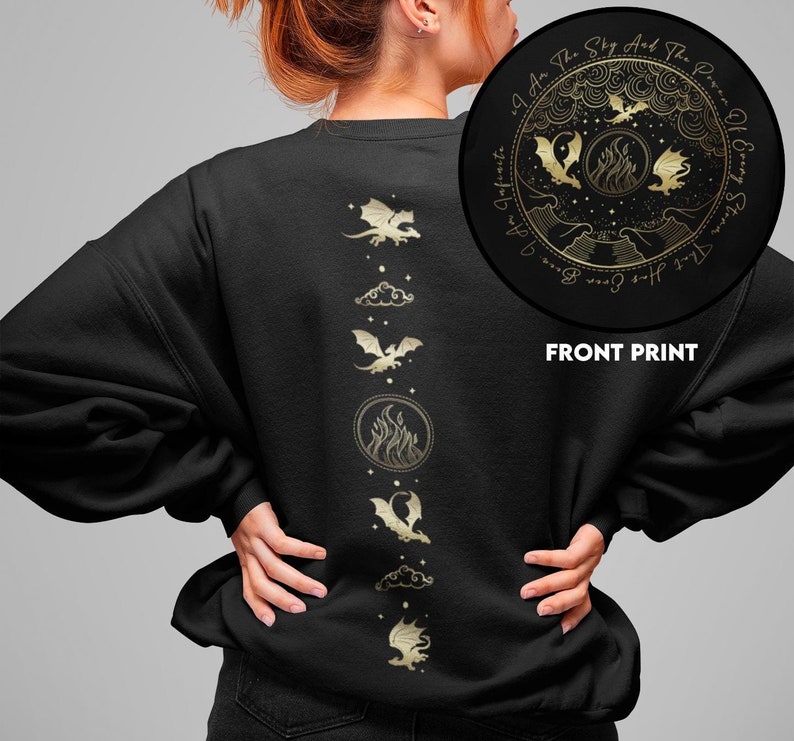 K&ouml;nnte beinhalten: Schwarzer Pullover mit einem goldenen Design auf der R&uuml;ckseite. Das Design zeigt eine Reihe von Drachen, Wolken und Flammen. Die Vorderseite des Pullovers hat ein kreisf&ouml;rmiges Design mit dem Text "I Am The Sky And The Power Of Every Storm That Has Ever Been. I Am The", in goldenen Buchstaben.