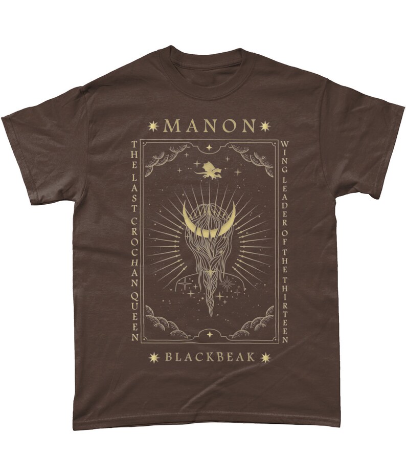 May include: A brown t-shirt with a gold graphic design featuring a crescent moon, stars, and the text "*MANON* THE LAST CROCHAN QUEEN WING LEADER OF THE THIRTEEN *BLACKBEAK*"