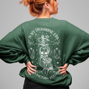 K&ouml;nnte beinhalten: Gr&uuml;ner Pullover mit einem wei&szlig;en Grafikdruck eines Sch&auml;dels mit einer Schlange, die um einen Dolch gewickelt ist. Der Text "In My Dramione Era In Fiction Reader" ist um die Grafik gedruckt.