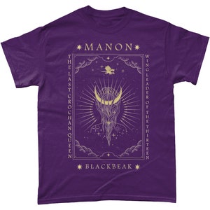 May include: Purple t-shirt with a gold design featuring a crescent moon, stars, and the text "*MANON* THE LAST CROCHAN QUEEN *BLACKBEAK* WING LEADER OF THE THIRTEEN"