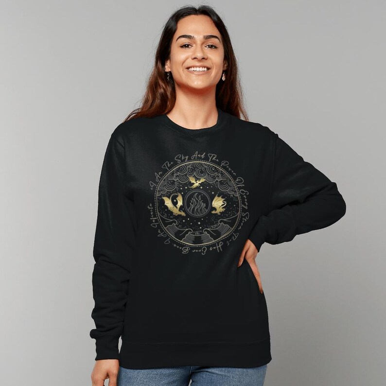 K&ouml;nnte beinhalten: Schwarzer Pullover mit einem goldenen Aufdruck von drei Drachen, die um ein Feuer fliegen, und dem Text "As To The Sky And The Power Of Every Star".