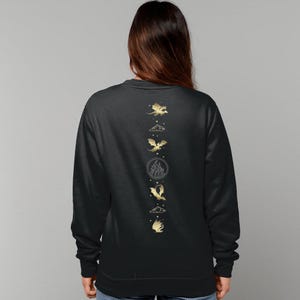 K&ouml;nnte beinhalten: Schwarzer Pullover mit einem goldenen Design aus f&uuml;nf Drachen in einer vertikalen Linie auf der R&uuml;ckseite. Die Drachen sind stilisiert und haben eine Wolke, Feuer und andere Elemente.