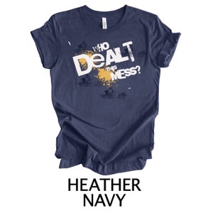 May include: Heather navy blue t-shirt with a white graphic that says "Who Dealt This Mess?" with a yellow splatter design.