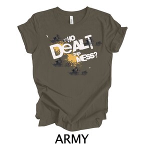 May include: Army green t-shirt with a white graphic that says "Who Dealt This Mess?" The graphic is in a distressed style with a yellow splatter effect.
