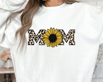 Op de afbeelding: Wit sweatshirt met een grafische print van het woord "MOM" in luipaardprint letters met een zonnebloem in het midden.