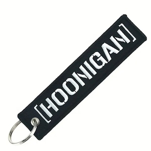 Pode incluir: Chaveiro preto com um texto bordado branco que diz "[HOONIGAN]".
