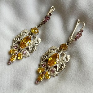 May include: A pair of silver dangle earrings with a filigree design and yellow and pink gemstones.
