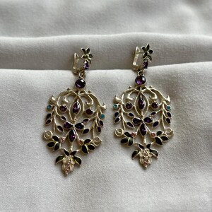 May include: A pair of silver dangle earrings with a floral design. The earrings are adorned with purple, pink, and turquoise gemstones.