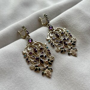 May include: A pair of dangle earrings with a gold filigree design and purple, green, and blue gemstones.