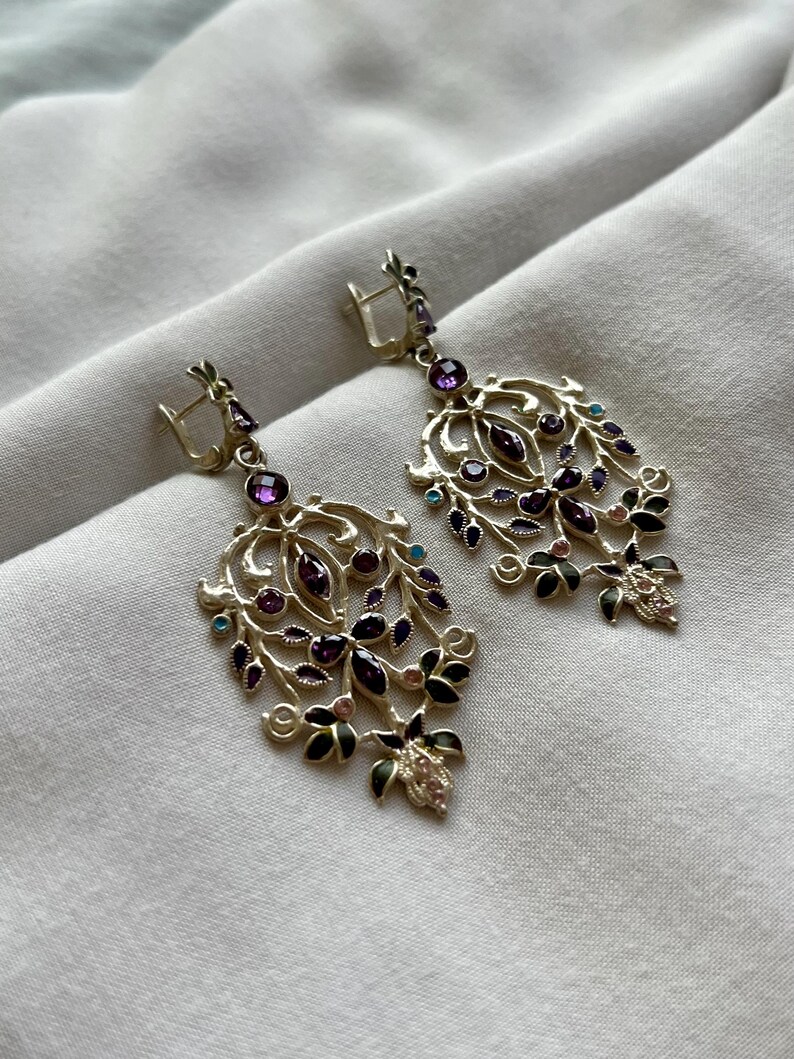 May include: A pair of dangle earrings with a gold filigree design and purple, green, and blue gemstones.