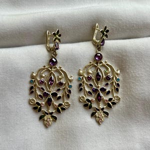 May include: A pair of silver dangle earrings with a floral design. The earrings are adorned with purple, pink, green, and blue gemstones.