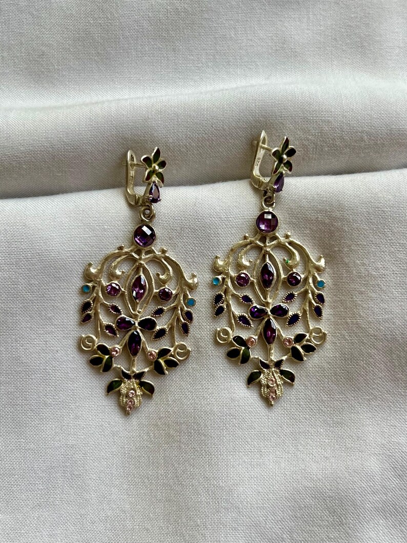 May include: A pair of silver dangle earrings with a floral design. The earrings are adorned with purple, pink, green, and blue gemstones.
