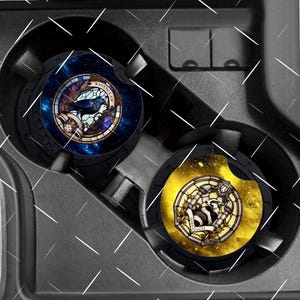 Peut inclure: Deux dessous de verre pour voiture avec des motifs circulaires. L'un représente un corbeau dans un style vitrail avec le mot "Ravenclaw". L'autre présente un blaireau dans un style vitrail avec le mot "Hufflepuff". Les deux sont noirs avec un bord texturé.