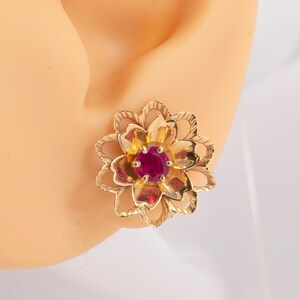 May include: Gold flower-shaped earrings with a red gemstone in the center.