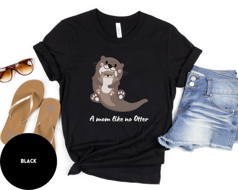 May include: Black t-shirt featuring a graphic of two otters hugging. The text "A mom like no Otter" is printed below the otters.