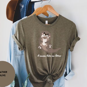 May include: A heather olive green t-shirt featuring a graphic of two otters hugging. The text "A mom like no Otter" is printed below the otters.