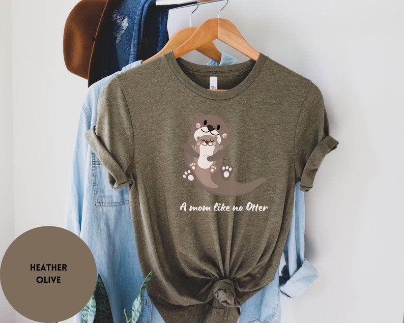 May include: A heather olive green t-shirt featuring a graphic of two otters hugging. The text "A mom like no Otter" is printed below the otters.