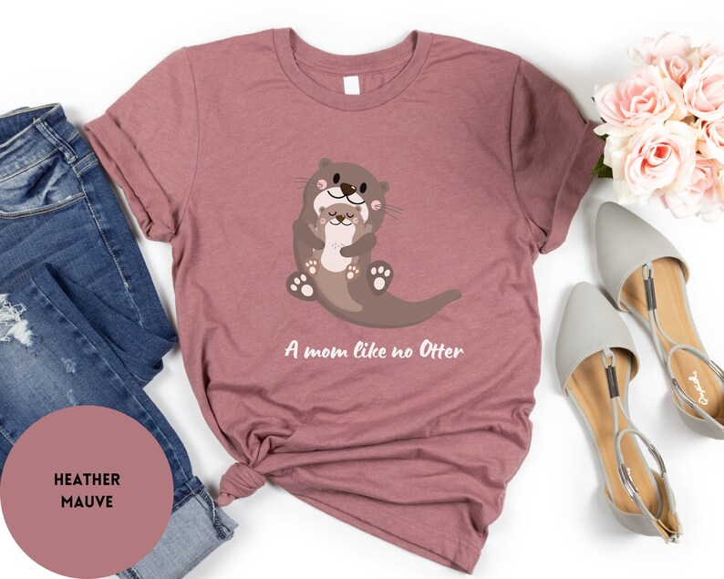 May include: A heather mauve t-shirt featuring a graphic of two otters hugging. The text "A mom like no Otter" is printed below the otters.
