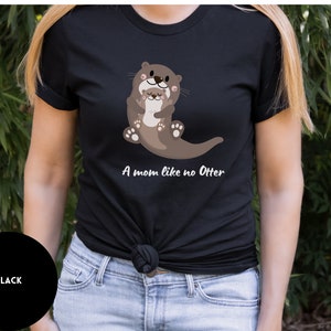 May include: Black t-shirt featuring a graphic of two otters hugging. The text "A mom like no Otter" is printed below the otters.
