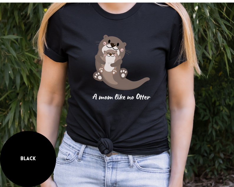 May include: Black t-shirt featuring a graphic of two otters hugging. The text "A mom like no Otter" is printed below the otters.