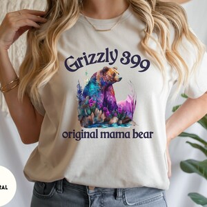 May include: A white t-shirt with a watercolor illustration of a grizzly bear with the text "Grizzly 399 original mama bear".