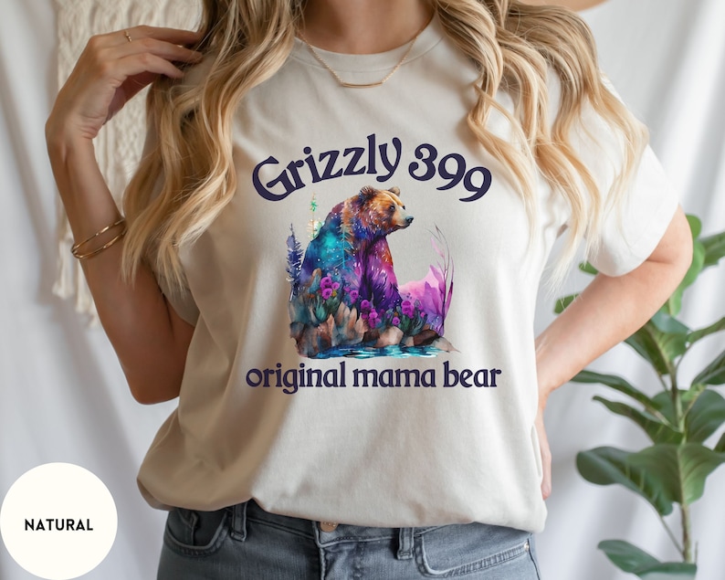 May include: A white t-shirt with a watercolor illustration of a grizzly bear with the text "Grizzly 399 original mama bear".