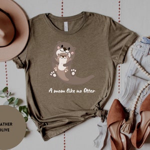 May include: A heather olive t-shirt featuring a graphic of two otters hugging. The text "A mom like no Otter" is printed below the otters.