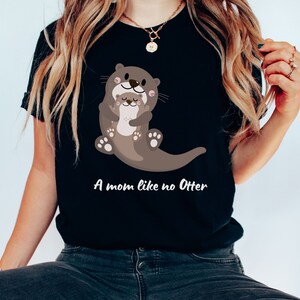 May include: A black t-shirt featuring a cartoon image of two otters hugging. The text "A mom like no Otter" is printed below the image.