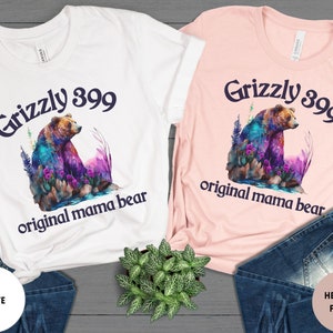 May include: Two t-shirts with a colorful grizzly bear graphic and the text "Grizzly 399 original mama bear". The shirt on the left is white and the shirt on the right is heather peach.