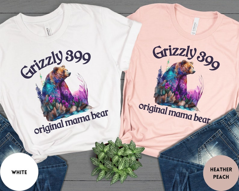 May include: Two t-shirts with a colorful grizzly bear graphic and the text "Grizzly 399 original mama bear". The shirt on the left is white and the shirt on the right is heather peach.