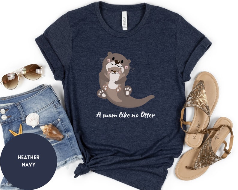 May include: Heather navy blue t-shirt featuring a graphic of two otters hugging. The text "A mom like no Otter" is printed below the otters.