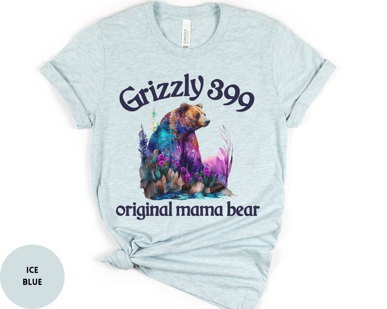 May include: Light blue t-shirt with a watercolor illustration of a grizzly bear in a forest setting. The text "Grizzly 399 original mama bear" is printed in navy blue.