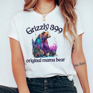 May include: White t-shirt with a colorful illustration of a grizzly bear and the text "Grizzly 399 original mama bear".