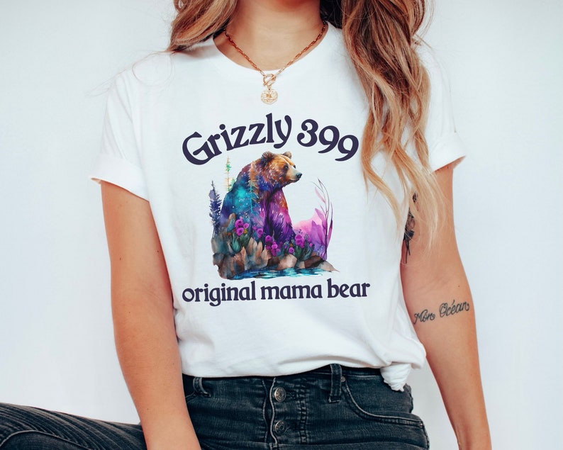 May include: White t-shirt with a colorful illustration of a grizzly bear and the text "Grizzly 399 original mama bear".