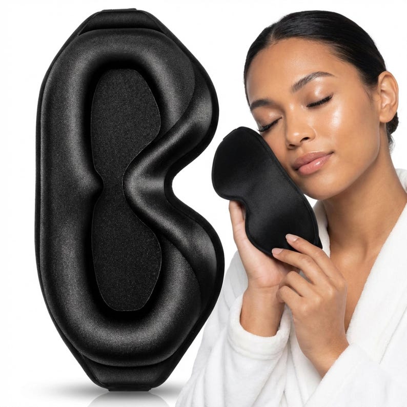 May include: A black sleep mask with a contoured design, next to a smaller, similar mask. The larger mask has a molded shape, while the smaller one appears to be made of a smooth, silky material. Both are designed for eye coverage.