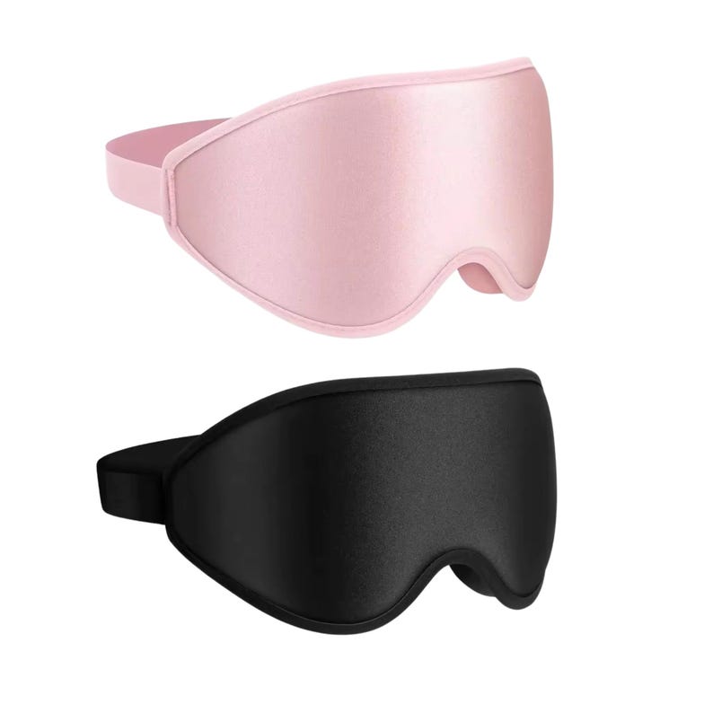 May include: Two sleep masks, one pink and one black, are displayed against a white background. The pink mask is a soft, light color, while the black mask is a deep, solid shade. Both masks have a contoured design and an elastic strap.