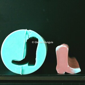 May include: A light blue silicone mold in a circular shape with a cowboy boot impression. A pink cowboy boot is next to the mold. The image includes the text "Glenda Munguia".