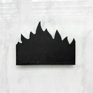 May include: A solid black, rectangular-based object with a jagged, flame-like top edge. The surface features a visible, diagonal 3D-printed texture pattern across the entire front face, creating a consistent matte finish throughout the piece.