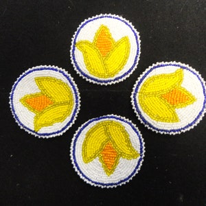 May include: Four round beaded coasters with a white background and a yellow flower design. The flowers have orange centers and are surrounded by a blue border.