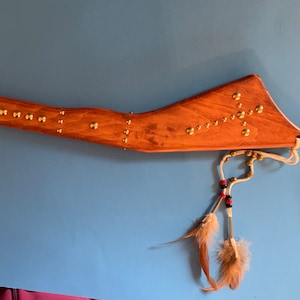 Könnte beinhalten: Ein hölzerner indianischer Kriegsclub mit Messingakzenten und einem weißen Lederriemen mit Perlen und Federn.